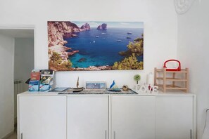 A room with a white cabinet, a painting of a coastal landscape, a small plant, and a red chair.