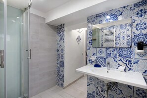 Un baño con ducha, lavabo y espejo, y azulejos azules estampados.