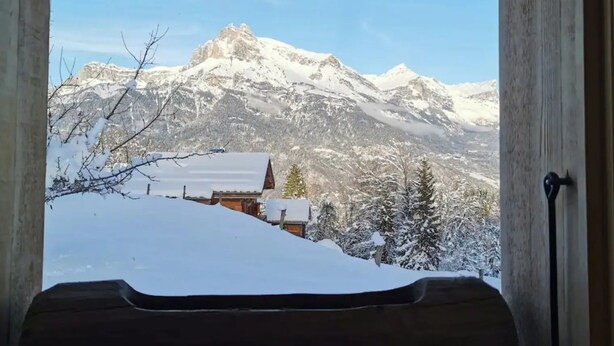A window with a view of snow-covered mountains and a wooden bench in the foreground. - Chalet 'Petit Cosy' with Mountain View, Wi-Fi and Air Conditioning (Combloux)