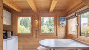 A wooden cabin interior with a kitchen, dining area, and large windows. - Chalet 'Petit Cosy' with Mountain View, Wi-Fi and Air Conditioning (Combloux)