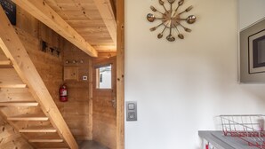 A wooden interior with a staircase, a wall-mounted clock, a fire extinguisher, and a kitchen area with a dish rack. - Chalet 'Petit Cosy' with Mountain View, Wi-Fi and Air Conditioning (Combloux)