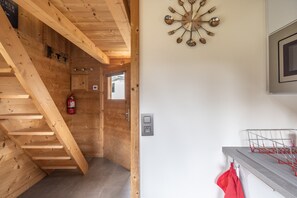 A wooden interior with a staircase, a wall-mounted clock, a fire extinguisher, and a kitchen area with a dish rack.