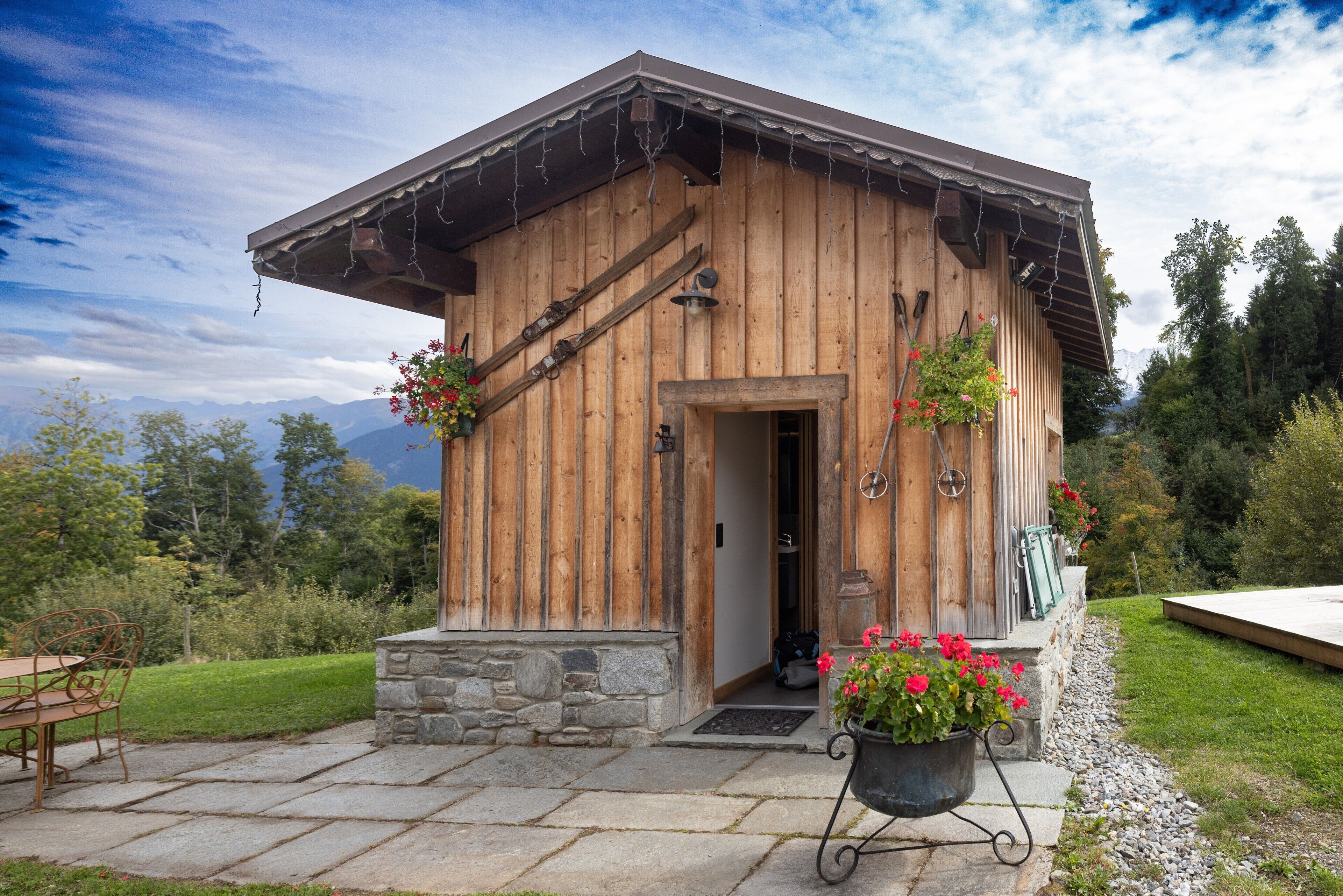A wooden cabin with a stone foundation, a door, and a small porch area with potted plants.