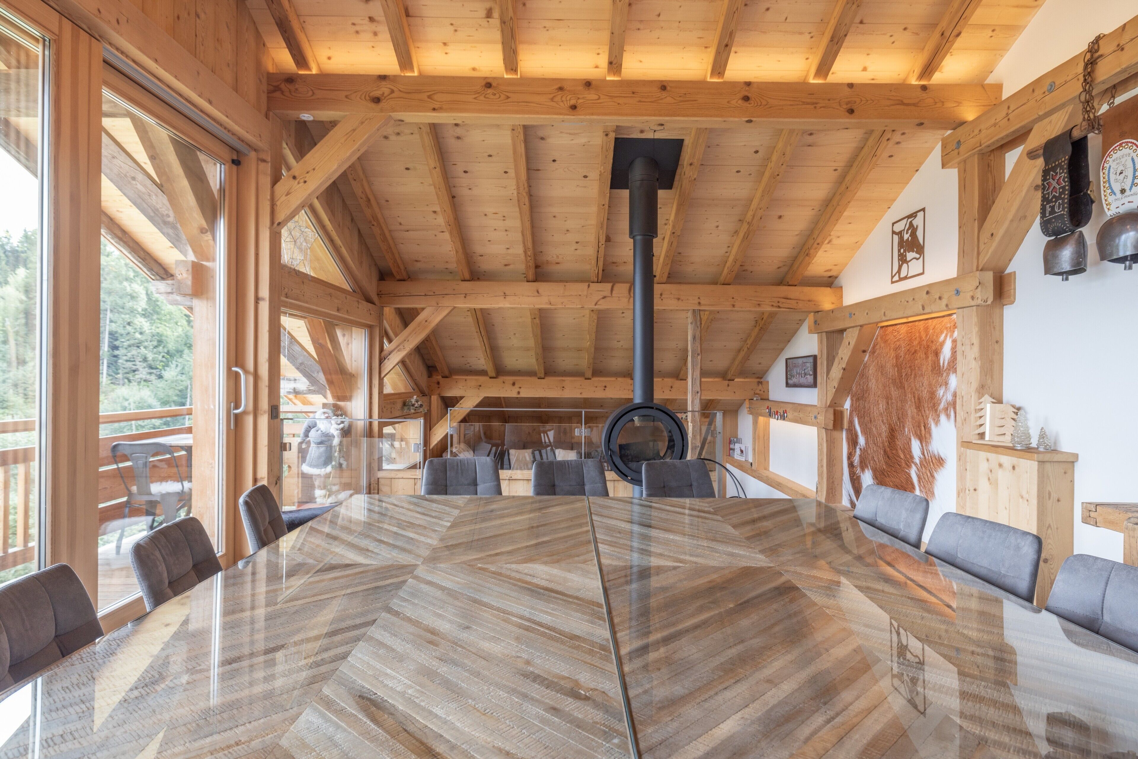 Un interno in legno con un tavolo rotondo grande, sedie e un soffitto alto con travi a vista.