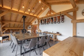 Un comedor espacioso con una larga mesa de madera, sillas grises tapizadas y un techo alto de madera con vigas a la vista y lámparas colgantes.