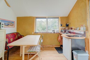A compact kitchen with a dining table, chairs, a bench, a window, and a small refrigerator. - Studio Apartment 'Gite 2 Personnes Sauna Et Étang' with Shared Garden and Wi-Fi (Broons)