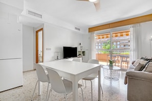 Una sala de estar moderna con una mesa de comedor blanca, sillas, un televisor y un sofá.