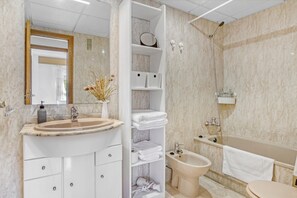 Une salle de bain moderne avec un lavabo en marbre, une étagère intégrée pour les serviettes, un bidet et une baignoire.