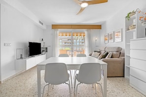 Un salon moderne comprenant une table à manger, des chaises blanches, un canapé, un téléviseur et un balcon avec vue.