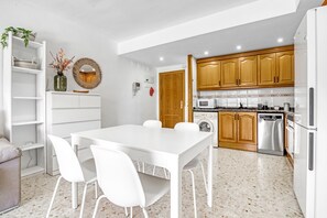 Una cocina moderna con armarios blancos, una mesa de comedor con sillas y un horno empotrado.