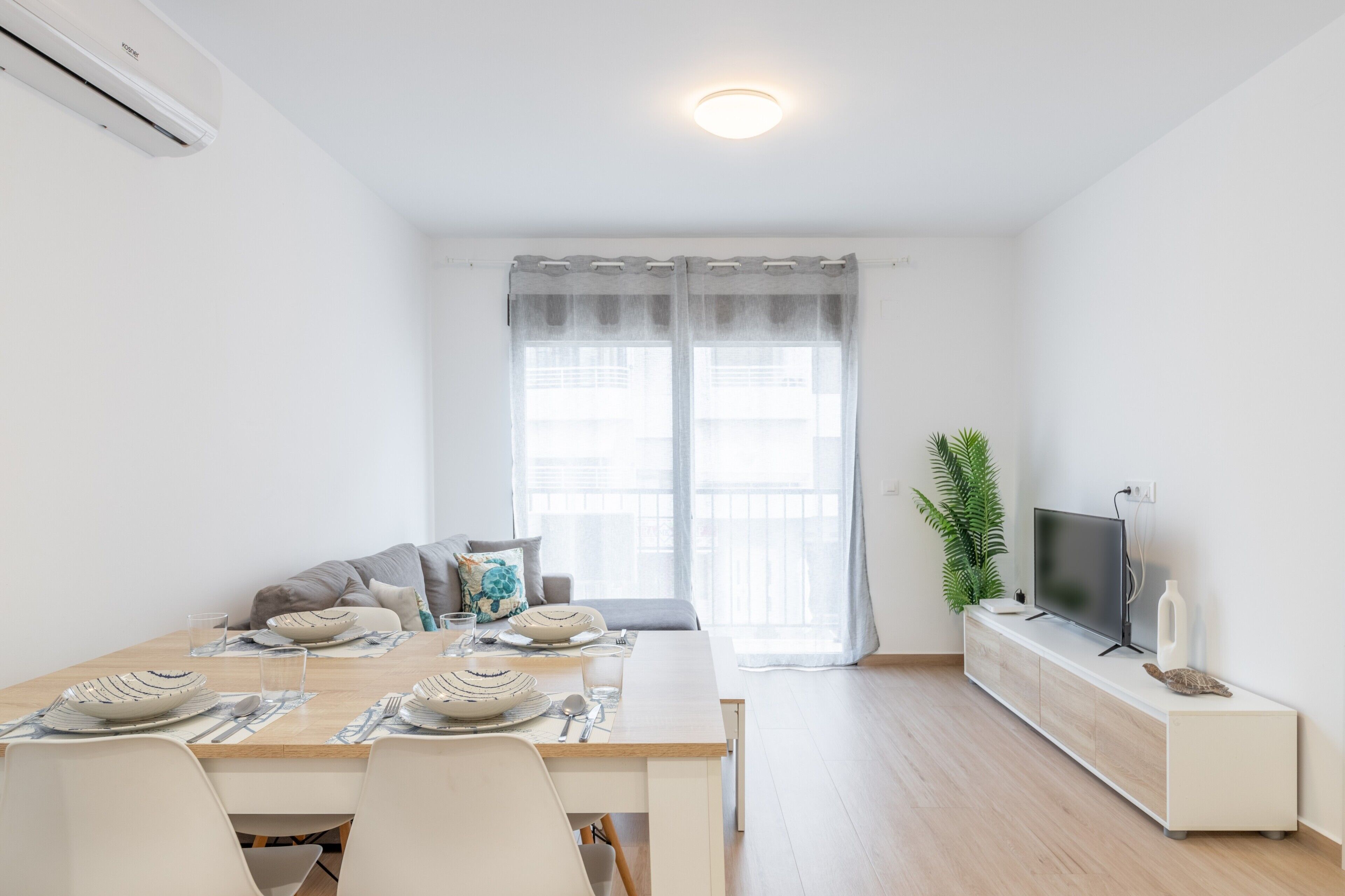 A modern living room with a dining area, a flat-screen TV, and a potted plant.