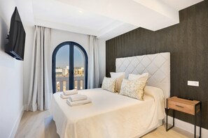 Ein Hotelzimmer mit einem großen Bett, einem an der Wand montierten Fernseher, einem Nachttisch aus Holz und Blick durch ein Fenster.