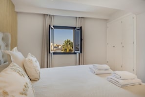 Una habitación de hotel con cama, ventana con cortinas y vistas a palmeras, además de un armario.