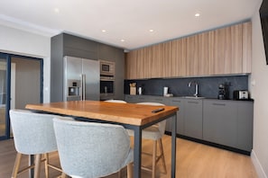 Una cocina moderna con una mesa de madera y taburetes de bar, electrodomésticos integrados y armarios grises.