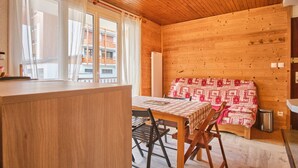 A wooden cabin interior with a dining table, chairs, a bench with a patterned cover, and a window with curtains. - Chez M & M Apartment – Balcony & Private Parking in Résidence Shrischss (Les Deux-Alpes)