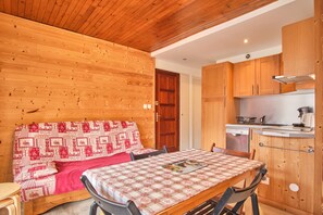 A wooden interior with a bed, a table, and a kitchen area. - Apartment 'Shrischss Joder' with Balcony (Les Deux-Alpes)