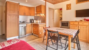 A compact kitchen with wooden cabinets, a dishwasher, a microwave, and a dining area with a table and chairs. - Chez M & M Apartment – Balcony & Private Parking in Résidence Shrischss (Les Deux-Alpes)