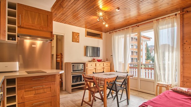 A compact kitchen with wooden cabinets, a built-in oven, and a dining area with a table and chairs. - Chez M & M Apartment – Balcony & Private Parking in Résidence Shrischss (Les Deux-Alpes)