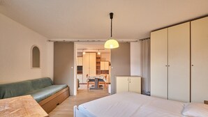 A bedroom with a bed, a green sofa, a wooden table, a wardrobe, and a kitchen area in the background. - Apartment 'Meijotel' with Mountain View and Balcony (Les Deux-Alpes)