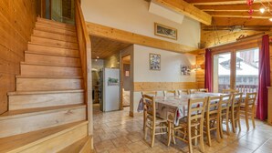 A wooden staircase leading to a dining area with a table and chairs, a refrigerator, and a view through a window. - Apartment 'Le Pelvoux' with Balcony (Les Deux-Alpes)