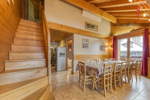 A wooden staircase leading to a dining area with a table and chairs, a refrigerator, and a view through a window.