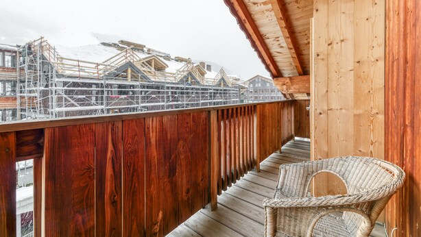A wooden balcony with a wicker chair, overlooking a building under construction with scaffolding. - Apartment 'Le Pelvoux' with Balcony (Les Deux-Alpes)