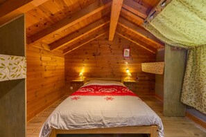 A wooden cabin bedroom with a bed, two bedside lamps, and a window with curtains.
