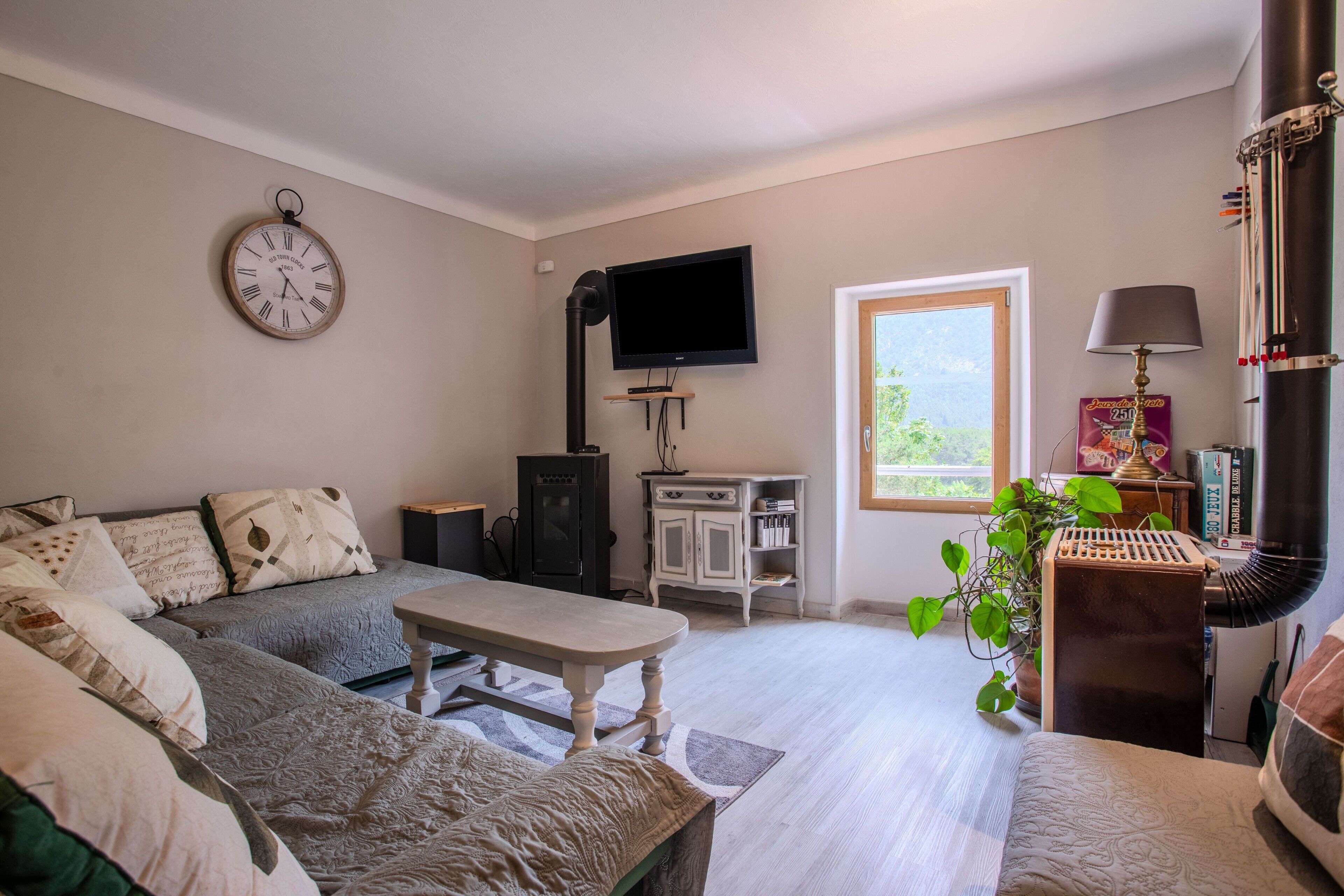 Un salon avec un canapé, une table, un téléviseur, une horloge et une fenêtre.