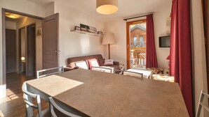 A room with a dining table, chairs, a sofa, a lamp, a TV, and a wooden door leading to an outdoor area.