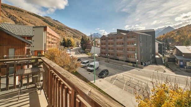 A hotel with a balcony, a street view, and mountains in the background.