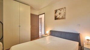 A bedroom with a bed, bedside table, lamp, and a door leading to another room.