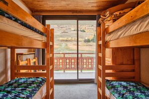 A bunk room with two beds, a view of a grassy landscape, and a wooden balcony.