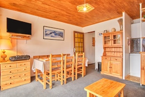 Une pièce avec un plafond en bois, un téléviseur, une table à manger avec des chaises, un buffet et un coin cuisine.