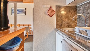 A kitchen with a granite countertop, stainless steel sink, and a black kettle on the stove.