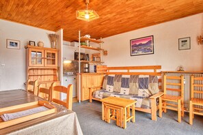 Une pièce chaleureuse avec un plafond en bois, un canapé recouvert d’une housse matelassée, une table à manger avec des chaises, un buffet en bois et un radiateur.