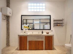 A modern bathroom with a large mirror, a wooden vanity, a built-in sink, and a small window above the mirror. - Berawa Factory Lofts (Canggu)