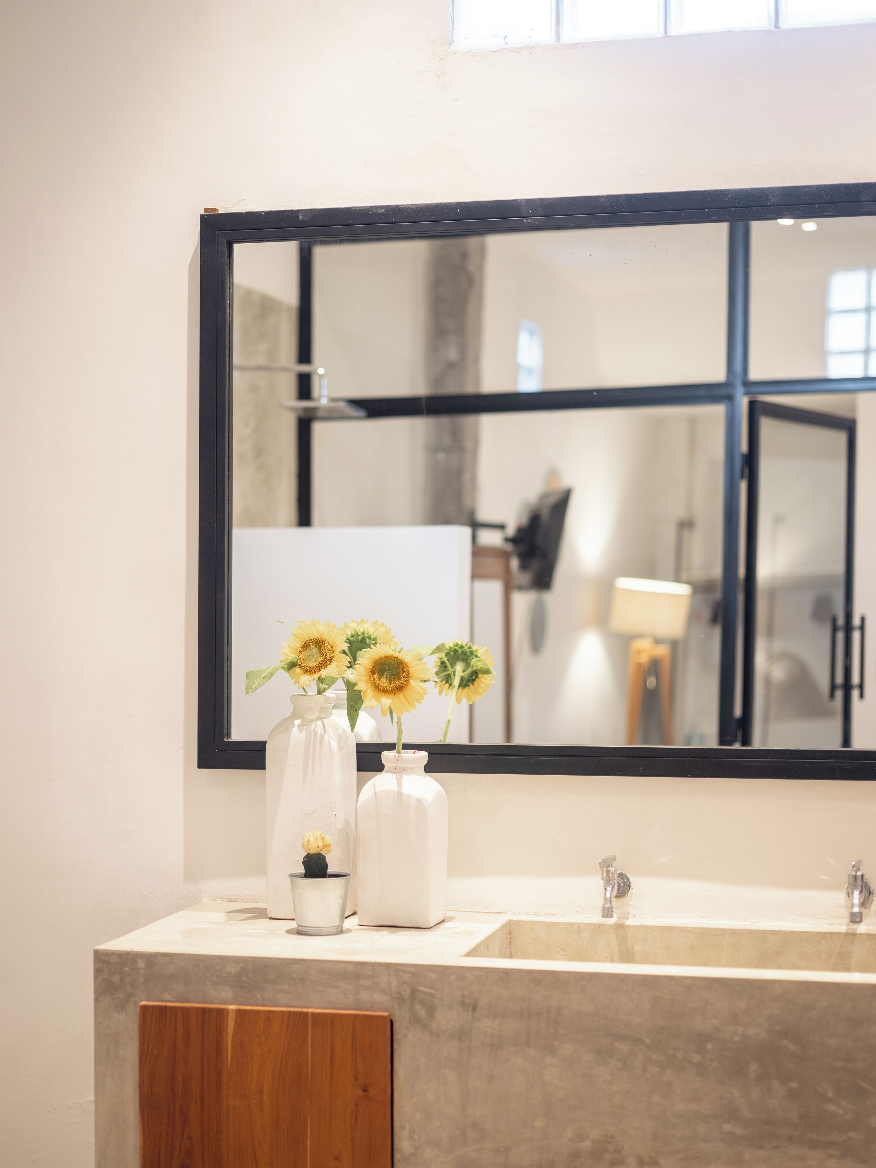 A bathroom with a large mirror, two sinks, and three vases with flowers on the countertop.