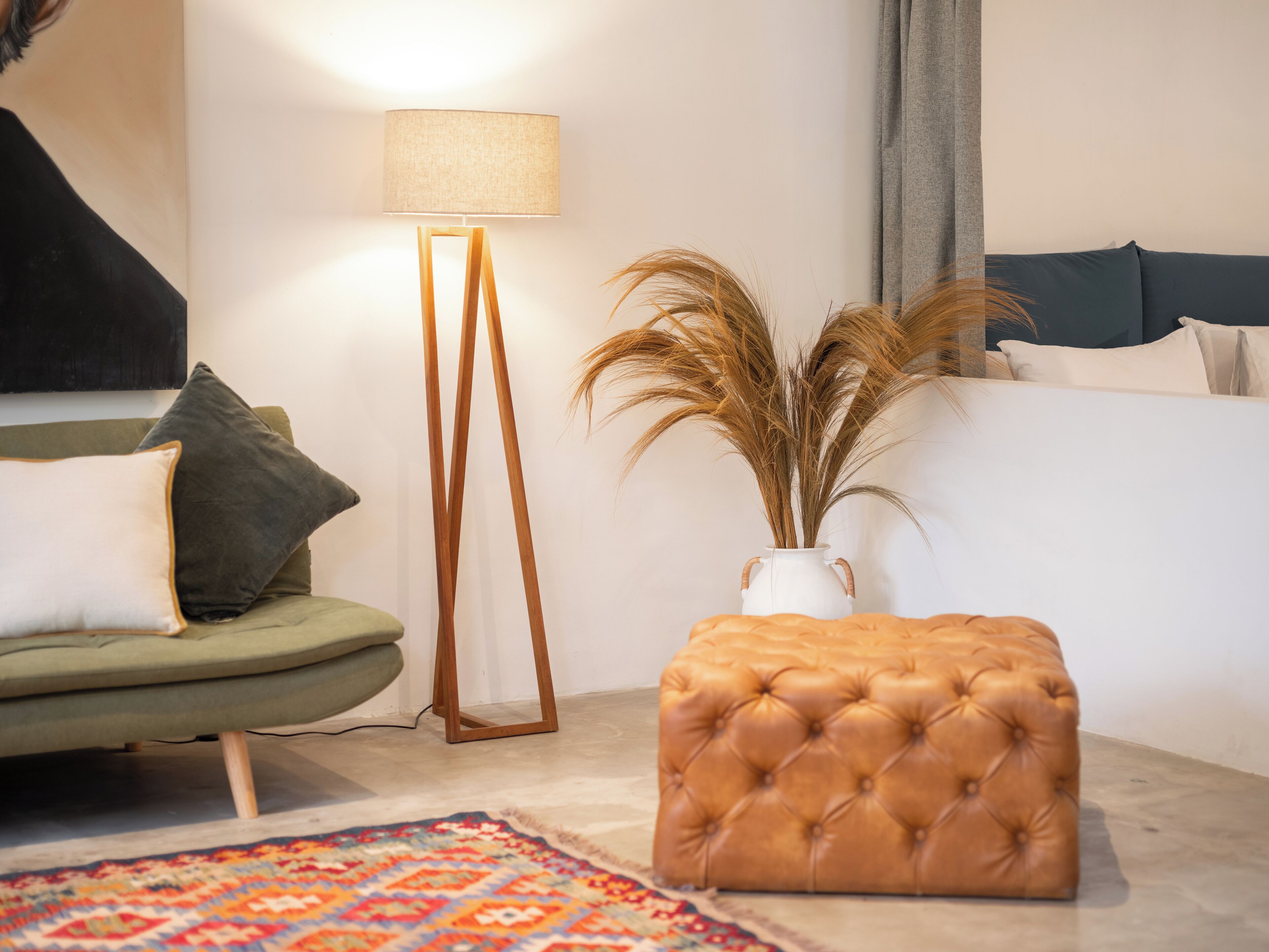 Un salon moderne avec un canapé vert, une lampe sur pied, un pouf capitonné et un vase contenant des plantes séchées.