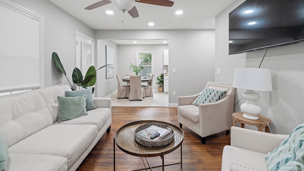 Un salon moderne doté d’un ventilateur de plafond, d’un téléviseur à écran plat, d’un coin repas avec une table et des chaises, et d’un espace salon confortable avec une lampe.