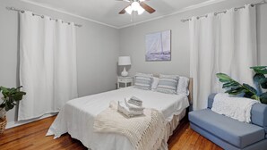 Une chambre à coucher avec un lit, un canapé bleu, un ventilateur de plafond, une table de chevet, une lampe et un tableau au mur.