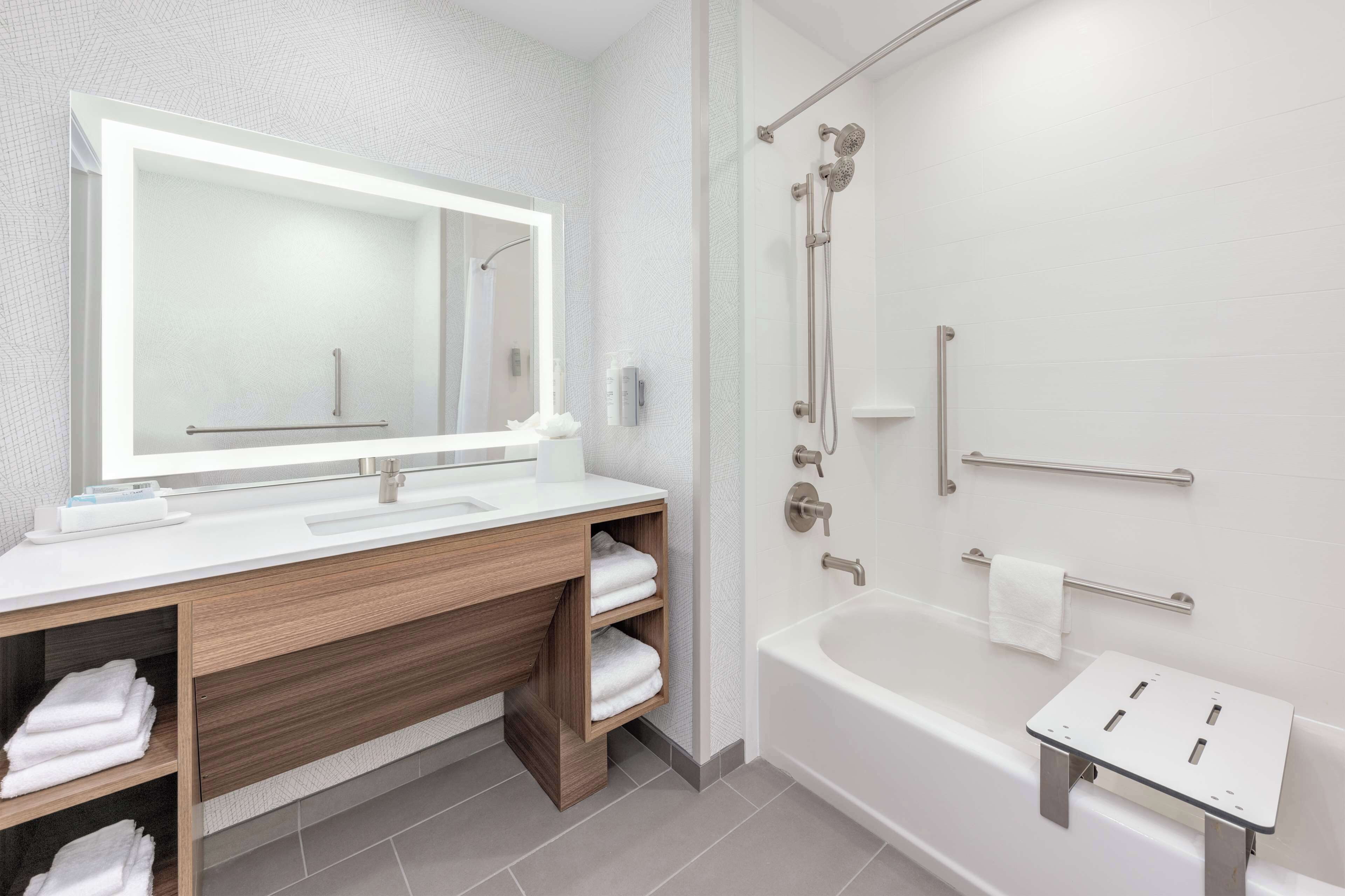 A modern bathroom with a large mirror, wooden vanity, white sink, and a separate shower area.