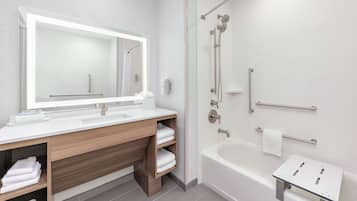 A modern bathroom with a large mirror, wooden vanity, white sink, and a separate shower area.