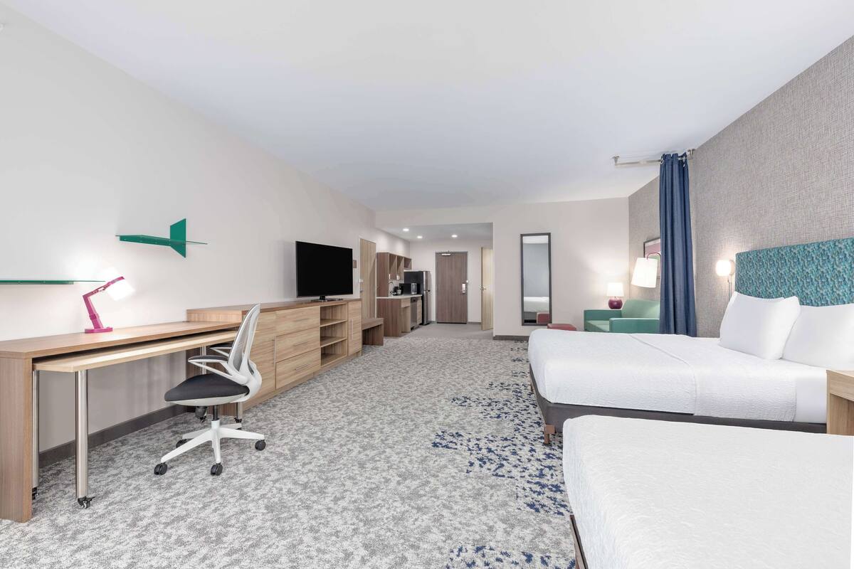 A hotel room with a desk, chair, two beds, a TV, a mirror, and a wardrobe.