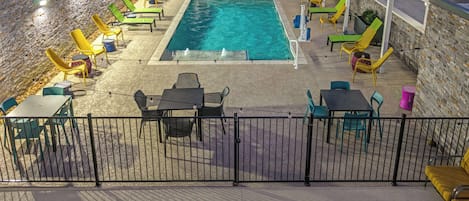A pool area with chairs and tables, surrounded by a stone wall and a covered section.