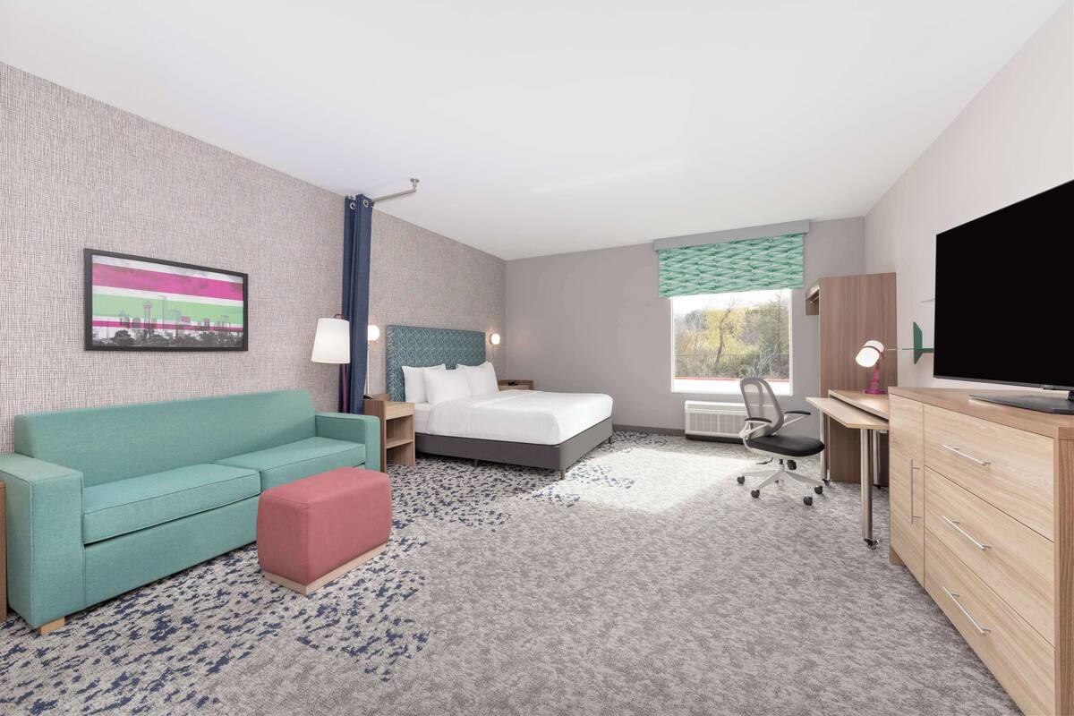 A hotel room with a bed, a desk, a TV, a couch, and a window with a view.