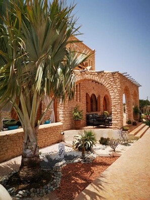 Un bâtiment en pierre, doté d’arches, avec un palmier au premier plan.