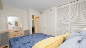 A bedroom with a bed, a dresser, a mirror, and a closet. - Cozy two bedroom, sleeps 6. Wifi, full kitchen, balcony, and pool. (Honolulu)