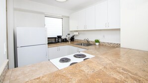 A modern kitchen with white cabinets, a white refrigerator, a stove, a sink, and a window with blinds. - Cozy two bedroom, sleeps 6. Wifi, full kitchen, balcony, and pool. (Honolulu)