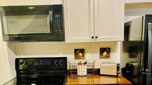 A compact kitchen with a microwave, stove, oven, and refrigerator. There are white cabinets and a wooden countertop.