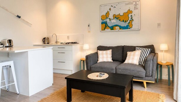 Ett modernt vardagsrum med en grå soffa, ett svart soffbord och en köksdel med vita skåp och en diskho.